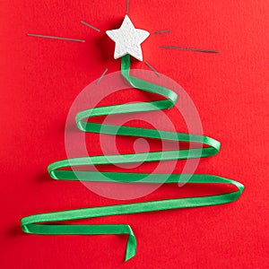 Christmas tree made of green ribbon with a burning white star on the red paper background