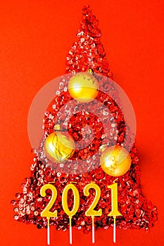 Christmas tree made by shiny confetti on red background. 2021 year gold candles. New Year and Merry Christmas greeting card