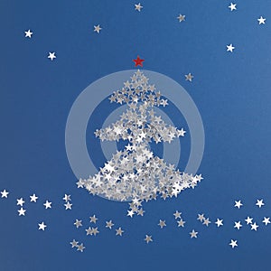 Christmas tree made of silver sequins in shape of stars. Christmas New Year composition. Blue background, selective focus, copy