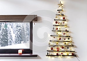 Christmas tree made of wood hanging on the wall, winter snowy landscape outside the window.