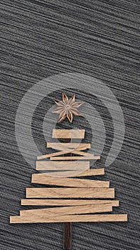 Christmas tree made of wooden boards and with cinnamon instead of a star on a dark fabric background.