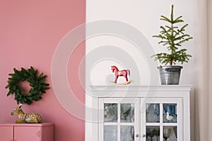 Christmas tree in a metal bucket, vintage wooden red toy horse on a white dresser in the interior of the living room, decorated