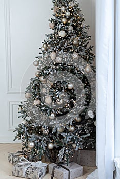 Christmas tree near the windows with gray-golden decorations and wrapped gifts under it