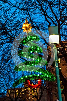 Christmas tree ornament hanging beside street lamp.