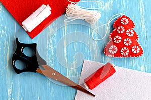 Christmas tree ornament, scissors, thread, needle, felt pieces on blue wooden background with empty place for text