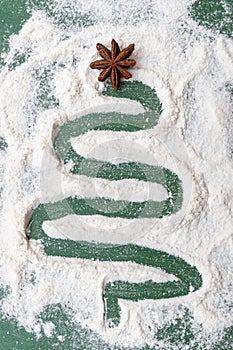 A Christmas tree painted from flour as from snow with a dried star of anise on a green background.