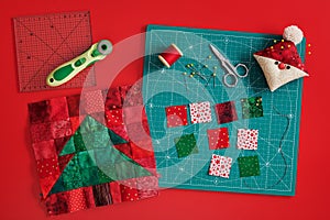 Christmas tree patchwork block, craft mat, bright square pieces of fabric, pincushion like Santa and quilting accessories on red