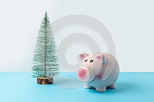 Christmas tree with piggy bank on blue table. Christmas or New Year minimal concept