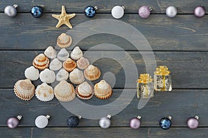 Christmas tree shape made from sea shells, two crystal giftboxes, decorative balls frame on wooden background,