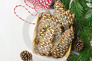 Christmas tree shaped shortbread cookies decorated with milk chocolate multicolored sugar sprinkles in wicker basket. Fir branches