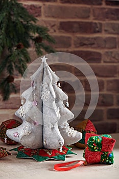 Christmas tree from silver cloth surrounded by soft decorative toys for Christmas tree on brick wall background