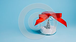 Christmas tree in snow closed in transparent jar with red bow tie satin ribbon on blue background. Creative Xmas eve