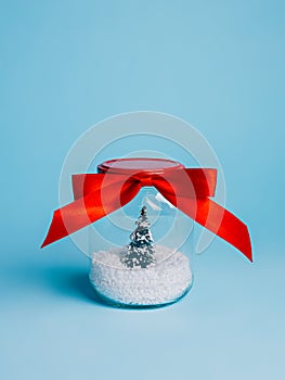 Christmas tree in snow closed in transparent jar with red bow tie satin ribbon on blue background. Creative Xmas eve