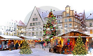 Christmas tree on town square in  old town of Tallinn and holiday marketplace  with walking people under snowflakes