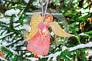Christmas tree toy in the form of an angel girl hangs on a snow-covered fir branch in the forest.