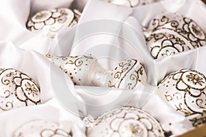 Christmas tree toys pearly balls and top painted golden glitter ornaments on a white silk cloth. Soft focus background