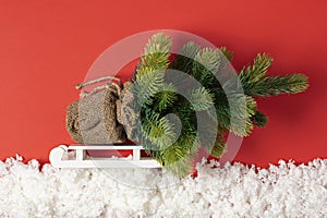 Christmas tree with toys on a sleigh in decorative snow. Christmas story on paper red background