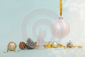 Christmas tree white ball hanging on a gold ribbon on a light blue background with Christmas balls, pine cones and gold