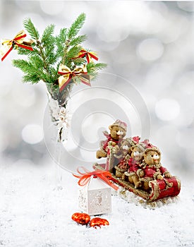 Christmas tree in white decorative goblet, white gift box, red and gold toy bears on sledge, candies and snow