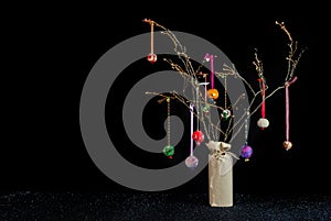 Christmas twig tree table decoration. Colourful baubles and black background.