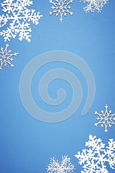 Christmas vertical composition with border of white decorative snowflakes on blue background. Flat lay, top view, copy