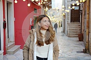 Christmas vibes. Portrait of winter woman walking between alleys decorated with lights in historic town