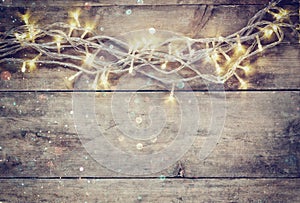 Christmas warm gold garland lights on wooden rustic background. filtered image with glitter overlay.