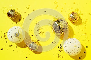 Christmas white and gold decorations, mirror disco balls, star sparkles over yellow background. Flat lay, top view. Minimal New