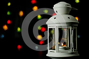 Christmas white lantern with a burning candle on the background of colorful lights garland, bokeh.