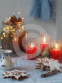 Christmas window. Candles, garlands, Christmas decoration, gingerbread cookie. Close-up, it is raining. Vertical orientation.