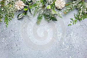 Christmas or winter background with a border of green and frosted evergreen branches and pine cones on a grey vintage board. Flat