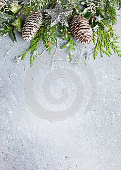 Christmas or winter background with a border of green and frosted evergreen branches and pine cones on a grey vintage board. Flat