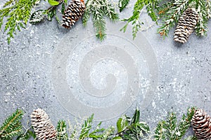 Christmas or winter background with a border of green and frosted evergreen branches and pine cones on a grey vintage board. Flat