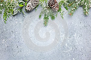 Christmas or winter background with a border of green and frosted evergreen branches and pine cones on a grey vintage board. Flat