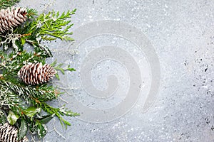 Christmas or winter background with a border of green and frosted evergreen branches and pine cones on a grey vintage board. Flat