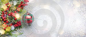 Christmas or winter background with a border of green and frosted evergreen branches, red berries and Christmas bauble on a grey