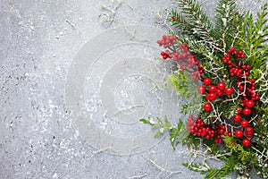 Christmas or winter background with a border of green and frosted evergreen branches and red berries on a grey vintage board. Flat