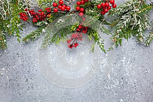 Christmas or winter background with a border of green and frosted evergreen branches and red berries on a grey vintage board. Flat