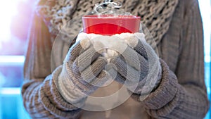 Christmas winter background - Young pretty woman with gloves and scarf stands on the balcony and holds a hot steaming teacup in