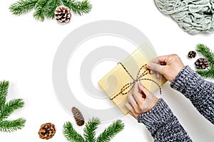 Christmas winter composition. Woman hands wrapping Christmas gifts box with pine cones, fir branches on white background. Flat lay