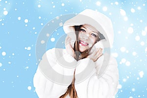 Christmas and winter holiday portrait of young woman in white hooded fur coat, snow on blue background, fashion and