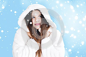 Christmas and winter holiday portrait of young woman in white hooded fur coat, snow on blue background, fashion and