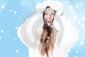 Christmas and winter holiday portrait of young woman in white hooded fur coat, snow on blue background, fashion and