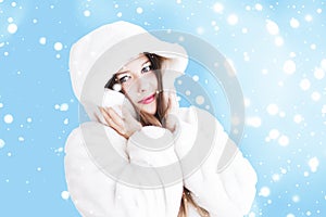 Christmas and winter holiday portrait of young woman in white hooded fur coat, snow on blue background, fashion and