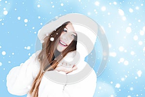 Christmas and winter holiday portrait of young woman in white hooded fur coat, snow on blue background, fashion and