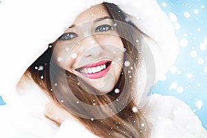 Christmas and winter holiday portrait of young woman in white hooded fur coat, snow on blue background, fashion and