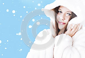 Christmas and winter holiday portrait of young woman in white hooded fur coat, snow on blue background, fashion and