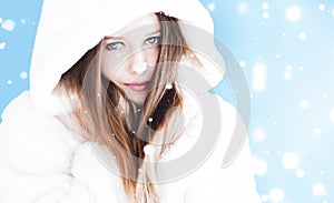 Christmas and winter holiday portrait of young woman in white hooded fur coat, snow on blue background, fashion and