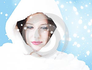 Christmas and winter holiday portrait of young woman in white hooded fur coat, snow on blue background, fashion and