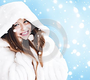 Christmas and winter holiday portrait of young woman in white hooded fur coat, snow on blue background, fashion and